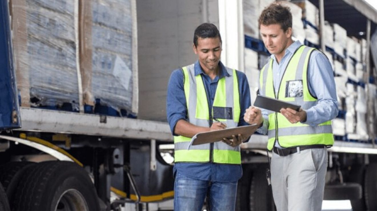 Dos trabajadores de transportes comparan los contenidos de un sujetapapeles con los contenidos de una tablet.